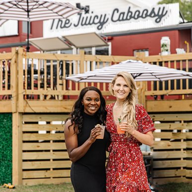 Two ladies holding a drink standing in front of their small business - The Juicy Caboosy
